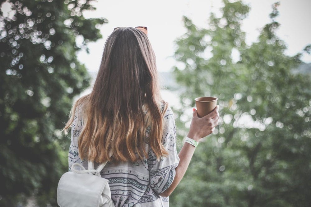 lugares que visitar en Canadá estudiante con pelo largo rubio de espaldas con café y mochila mirando la naturaleza de Canadá